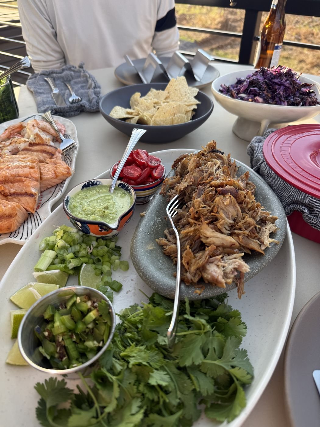 A taco spread on an outdoor table: carnitas, salmon, herbs and salsas